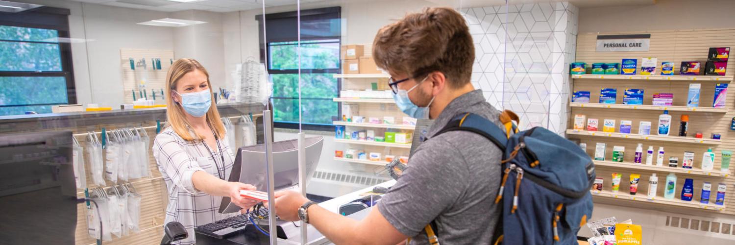 A student standing at the Apothecary Pharmacy checkout counter with a prescription medication and his insurance card.