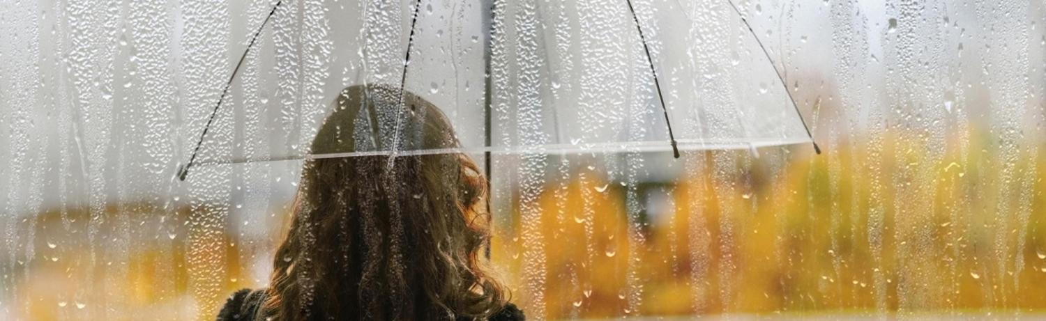 Woman in yellow rain jacket standing with a clear umbrella in the rain.