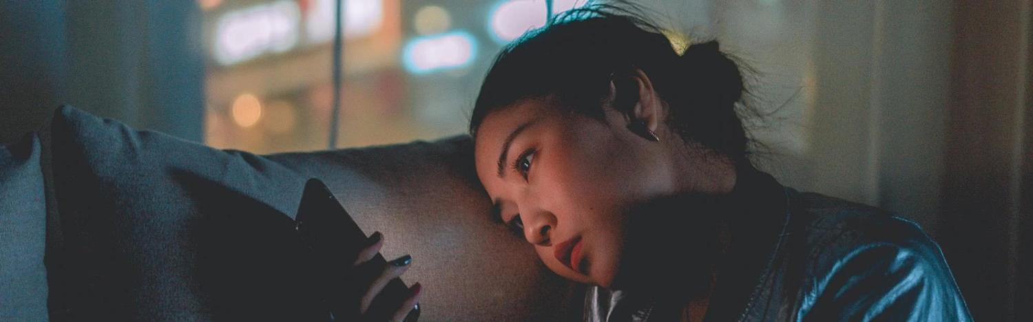 Student sitting in the dark with her phone as it illuminates her face on the couch.