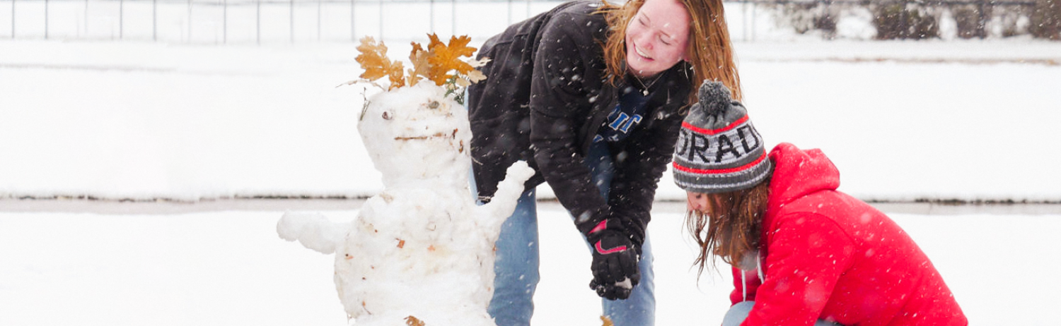 Photo of two students building a snowman outside on campus.