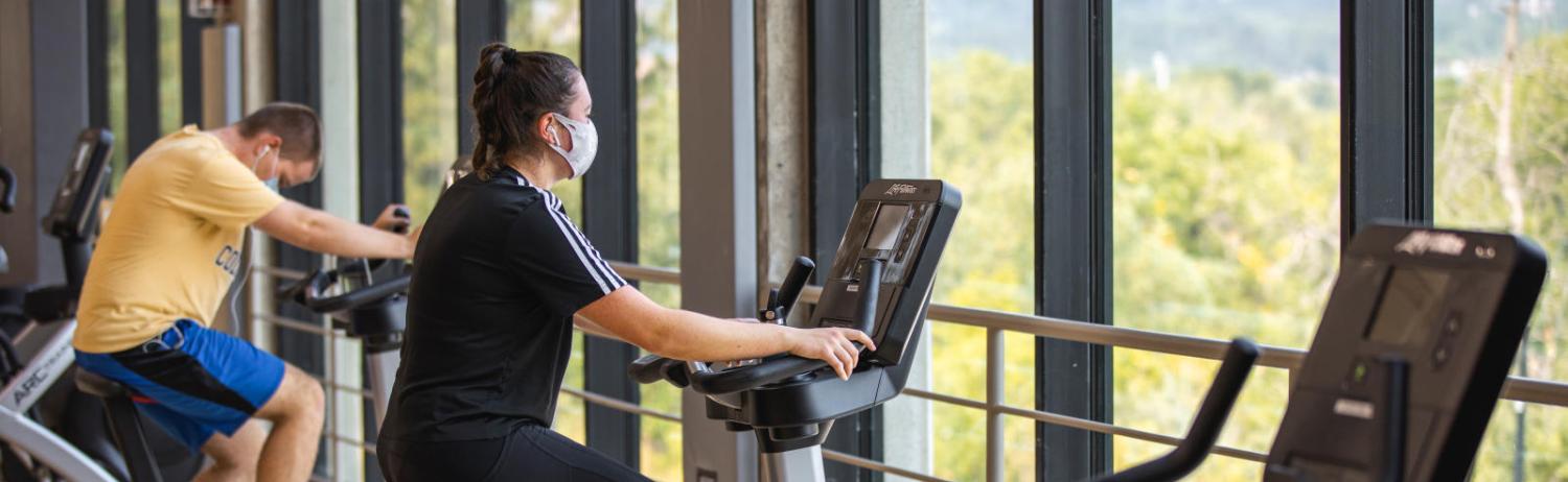 Two students riding stationary bikes on the top floor of the Rec Center.