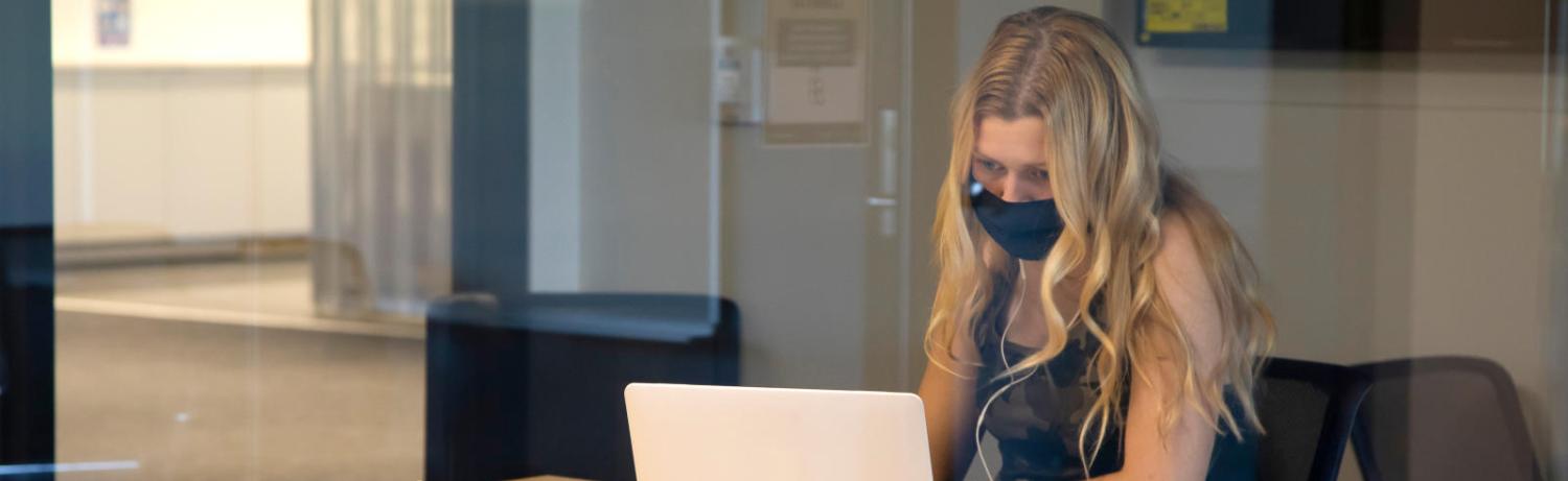 Grad student with long hair in a mask looking intently at her laptop.