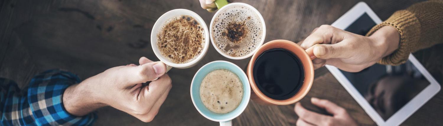 four friends cheering their coffee mugs in a cafe