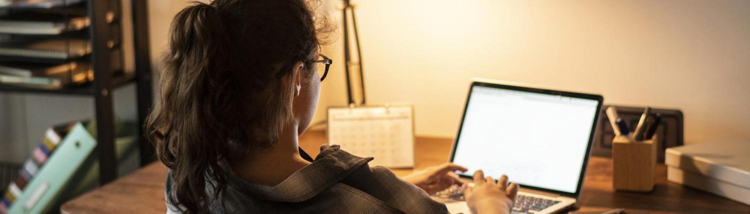 Student working on laptop at home with a lamp-lit desk.
