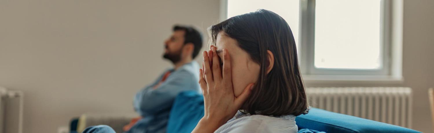 Girl sitting on the couch next to a guy with her hands over her face in frustration.