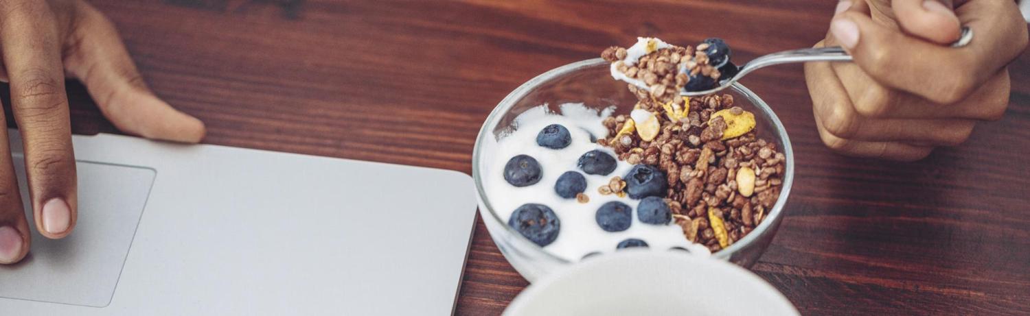 Person eating yogurt, berries and granola while on a laptop.