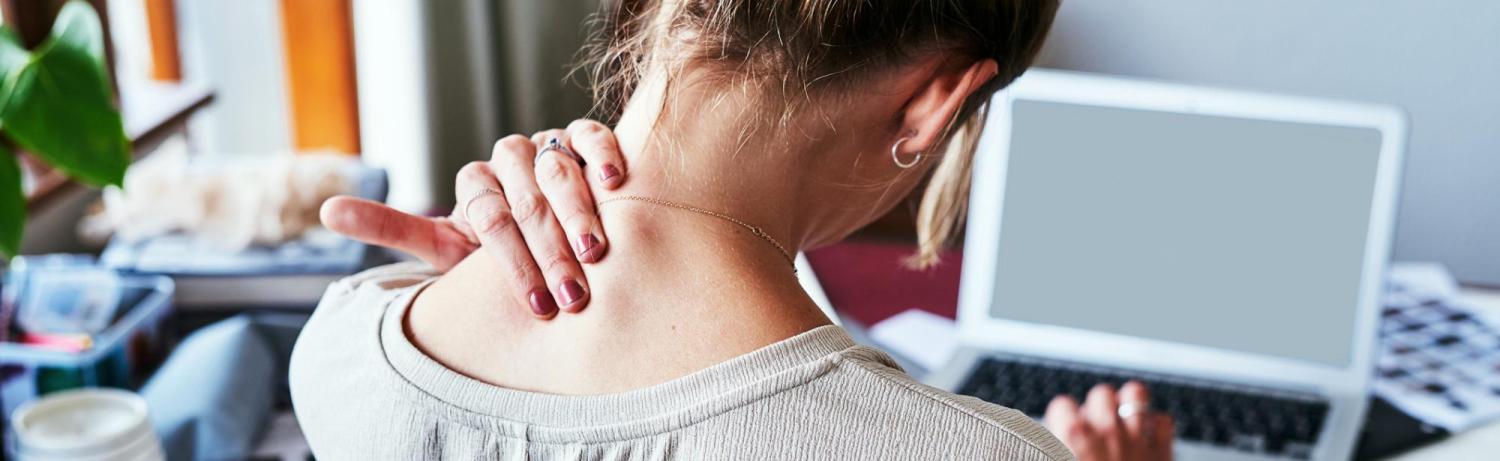 Girl rubbing her neck with discomfort while she works at a messy desk.