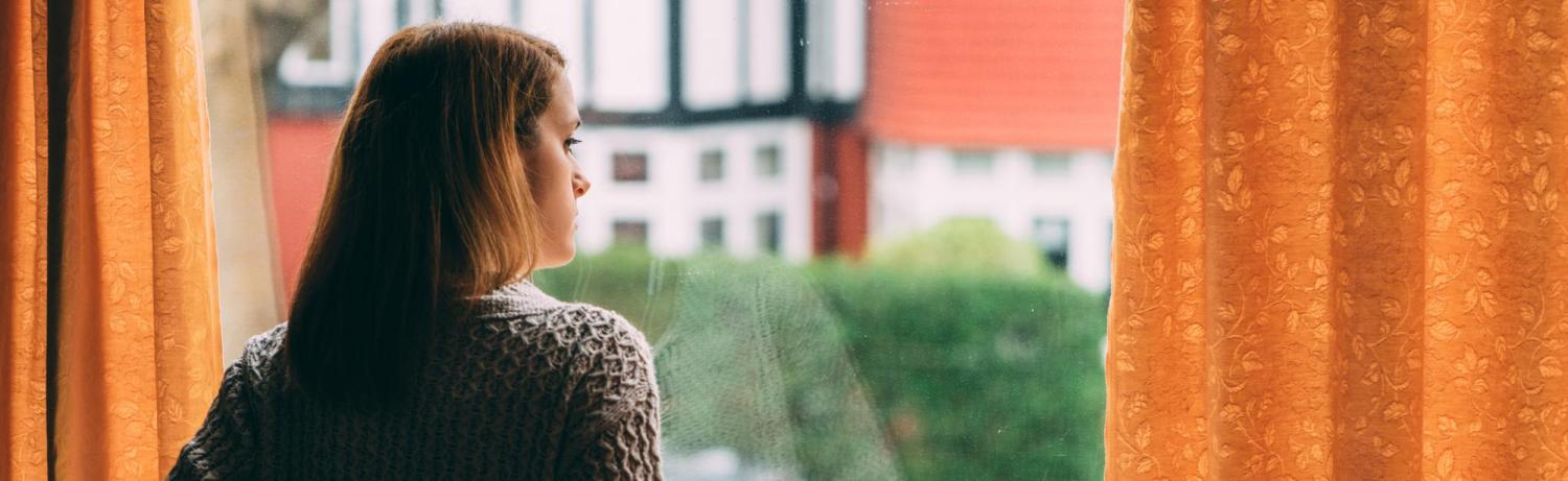 Girl staring out the window of her apartment on a gloomy day.