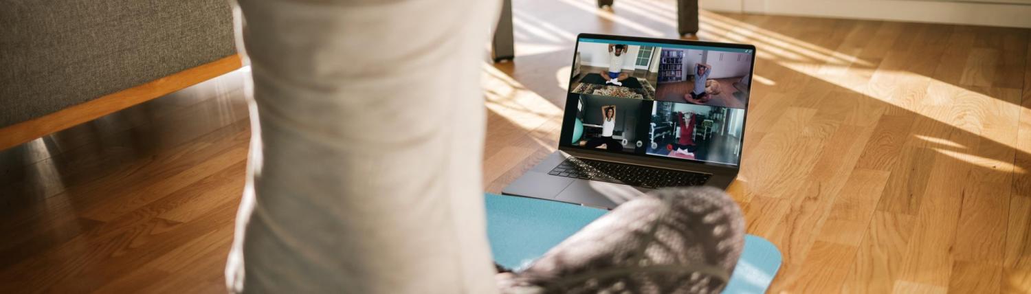 Woman sitting on yoga mat in front of live group chat video.