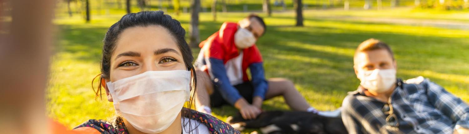 Girl taking a selfie wearing a mask in the park with her friends