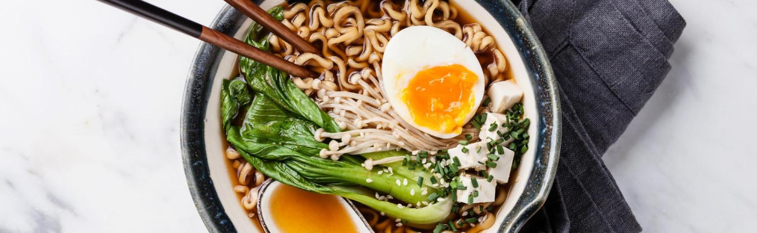 Bowl of ramen noodles in broth with eggs, seaweed and bok choy