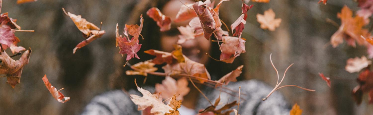 Girl throwing colorful fall leaves in the air in front of her face.
