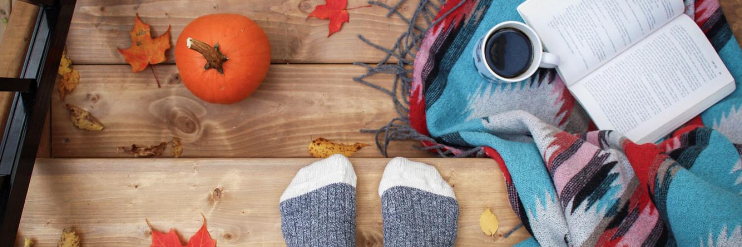 Person in socks standing on a deck with a journal and pumpkin
