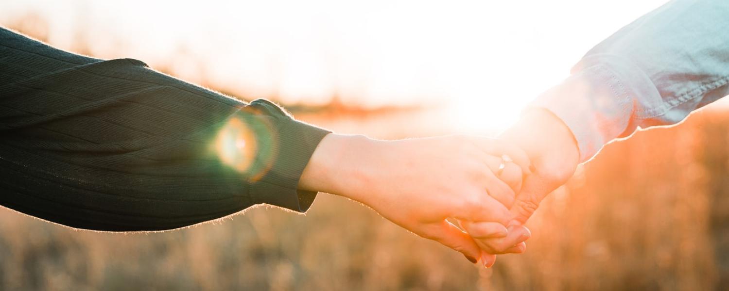 Two people holding hands in front of sunset