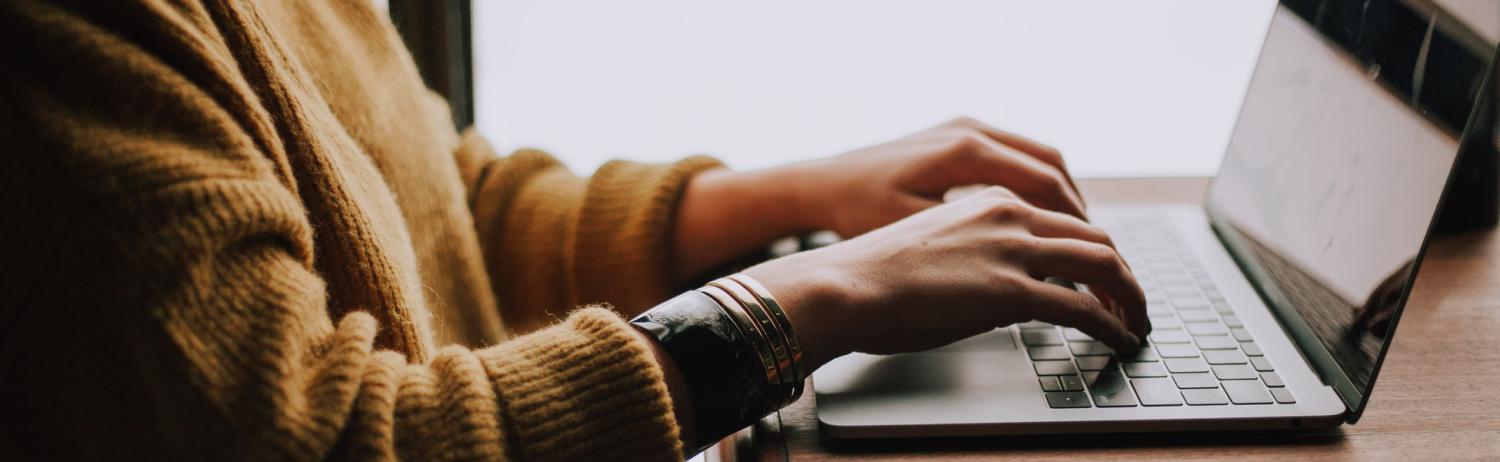 Person in a fuzzy sweater types on a laptop.