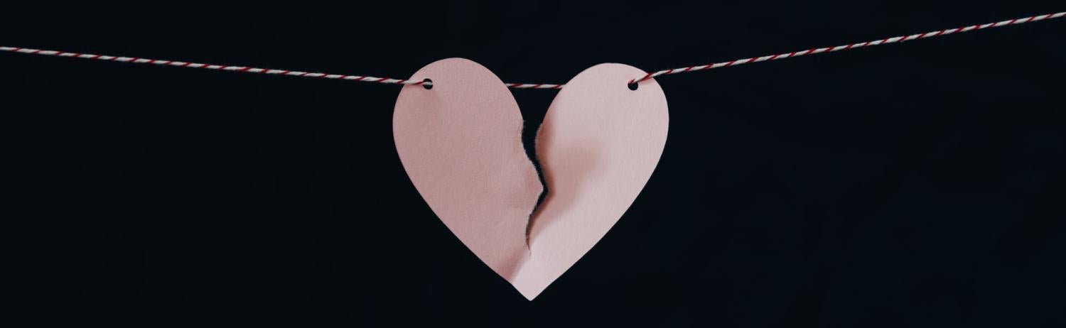 A paper heart ripped in half suspended on a string over a dark background.
