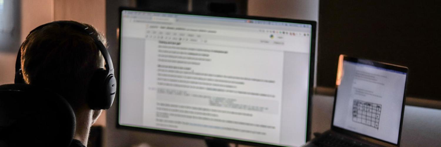 Guy studying on dual monitors late at night wearing headphones