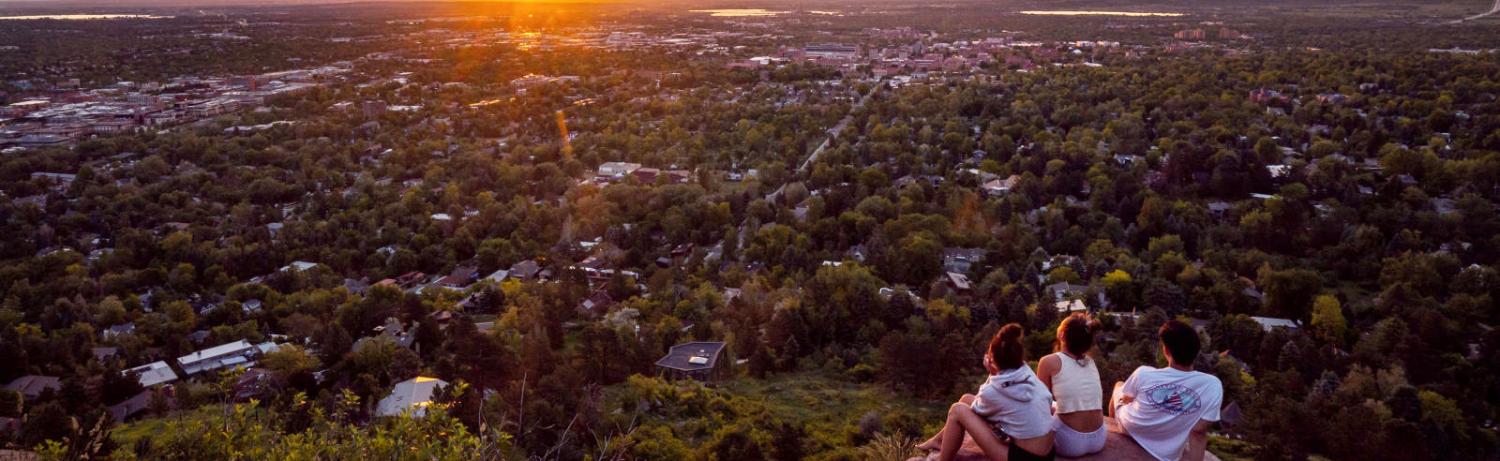 Three students sitting on a rocky hillside overlooking Boulder at sunset.