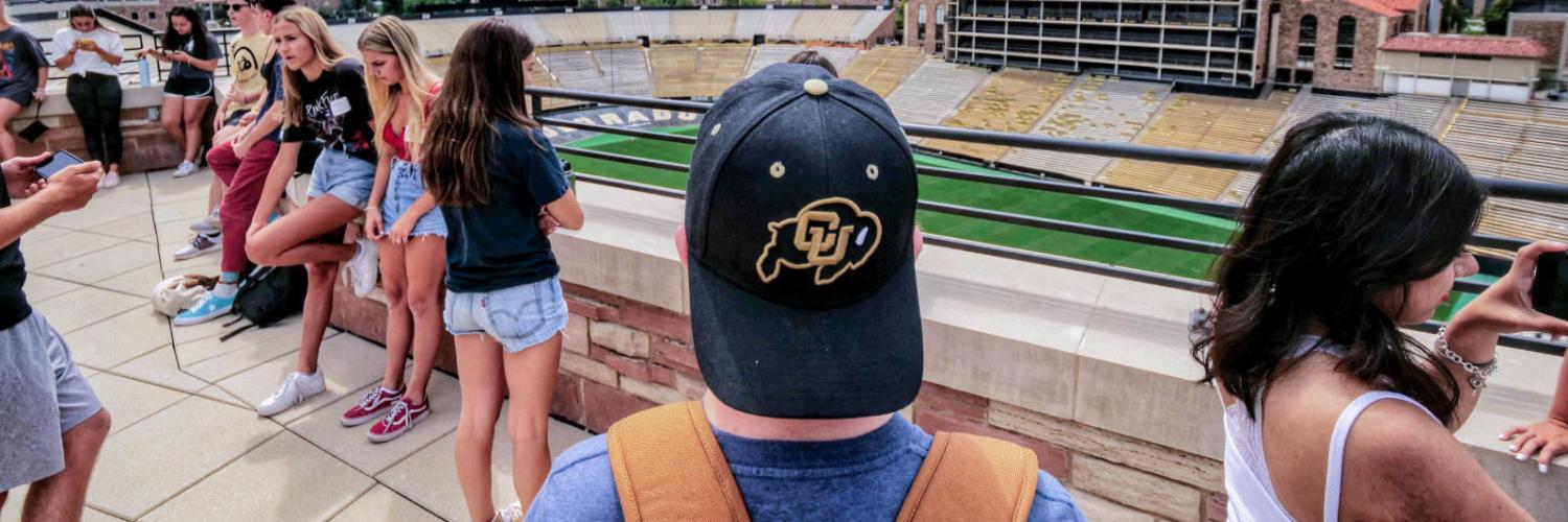 Student with black CU Ralphie hat looks out over Folsom field observation deck at the flatirons.