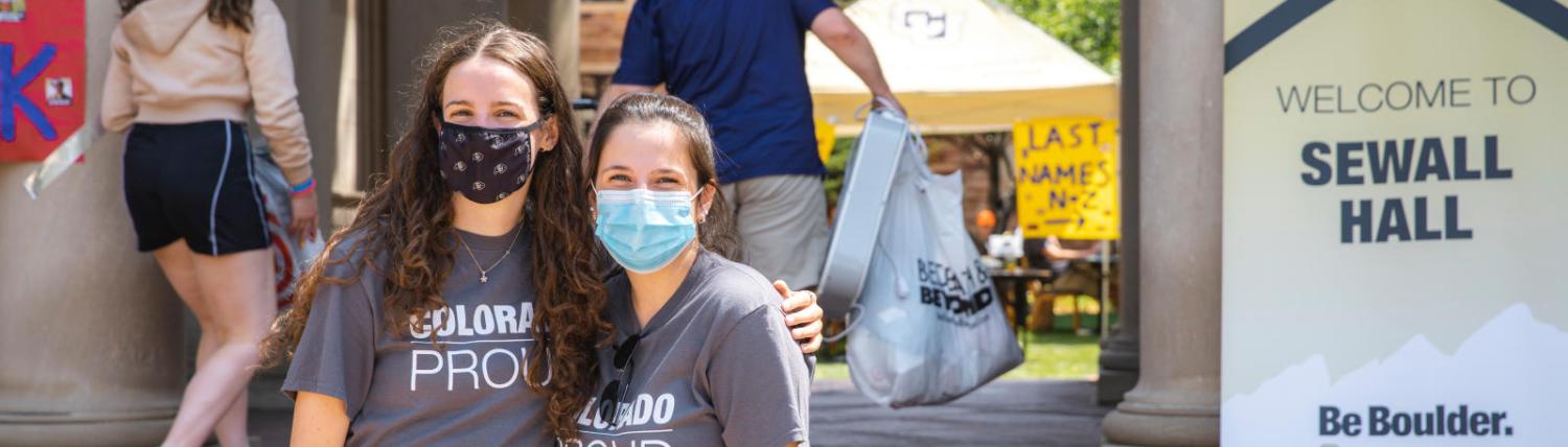 Two female students in masks standing in front of Sewall Hall wearing Colorado Proud t-shirts.