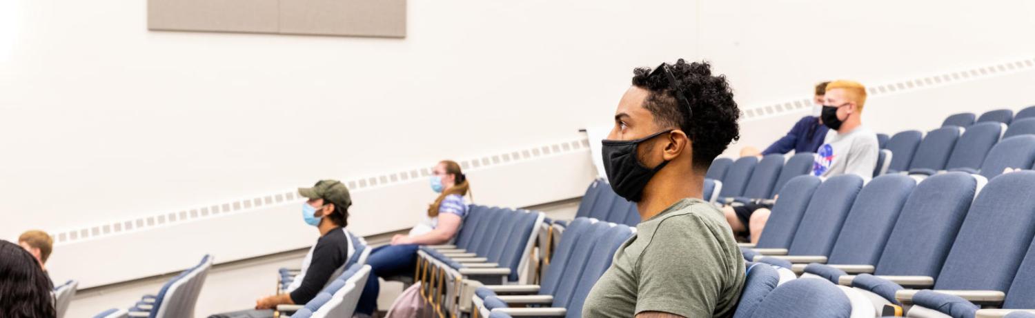 Students in masks sitting in a large lecture hall.