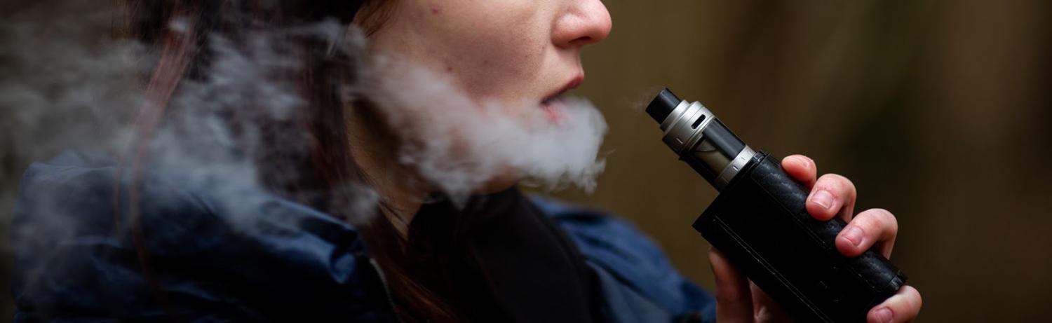 Girl holding a box vape while exhaling vapor on a cold day.