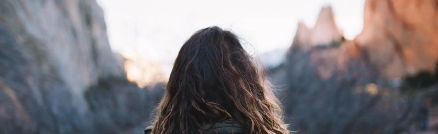 Photo of a girl looking out on a range of mountains at sunset.