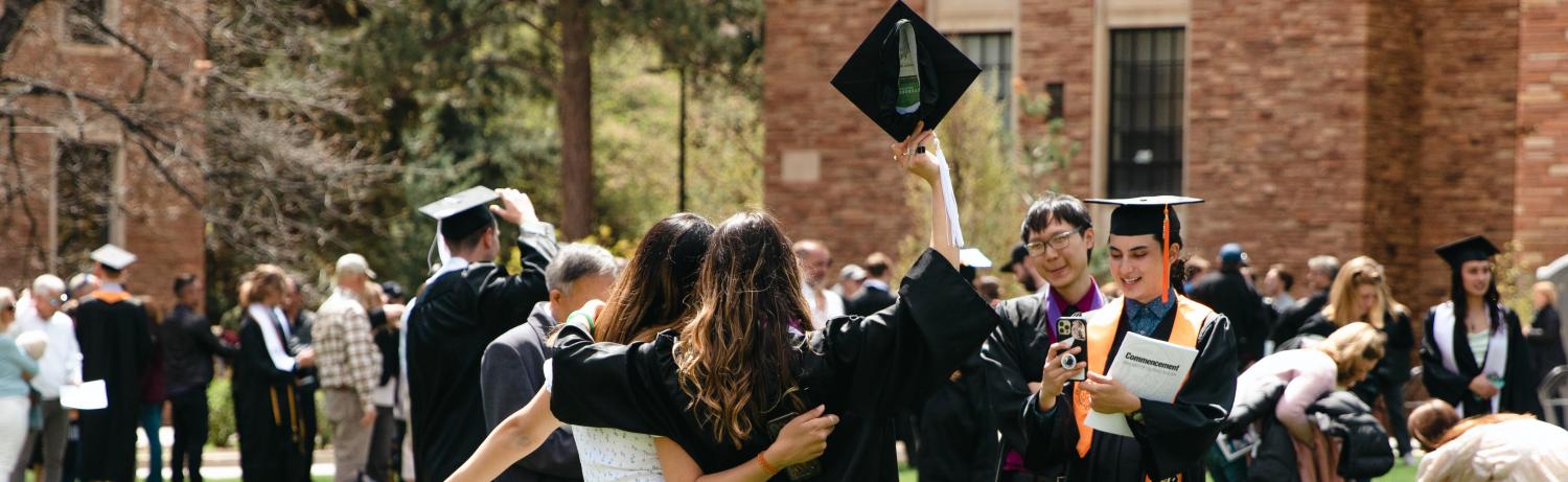 Photo of students posing for a photo with their graduation caps raised above their heads.