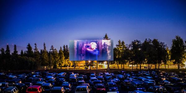 Photo of cars parked in the dark in front of a screen showing a horror film at the 88 Drive In Theater.