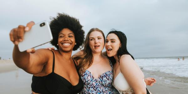 Photo of three friends posing in swimsuits on the beach.