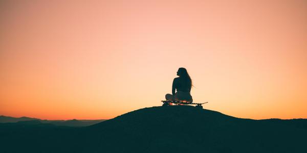 Photo of a girl sitting on a skateboard at sunset.