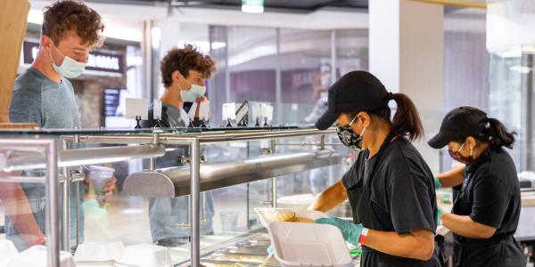 Campus dining staff serving food to students at a dining hall. 