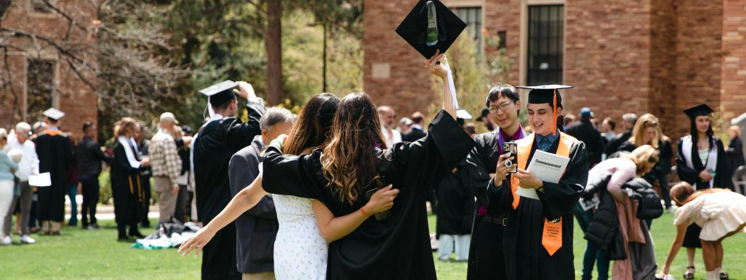 Photo of students posing for a photo with their graduation caps raised above their heads.