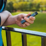 Person holding a vape pen outside in front of a grassy lawn.