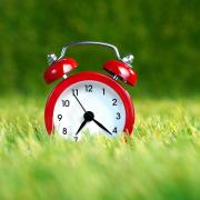 Photo of an old fashioned clock in a meadow of grass.