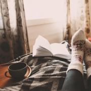 Photo of a person snuggled up with a dog, a book and cozy socks.
