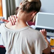 Girl rubbing her neck with discomfort while she works at a messy desk.