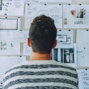 Student staring at a wall full of sticky notes and other pages of work.