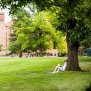 Photo of a student stretching under a tree while studying on Farrand Field.