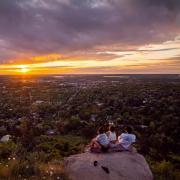 Three students sitting on a rocky hillside overlooking Boulder at sunset.
