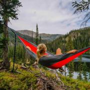 Blonde student with a pony tail lounges in a hammock overlooking a wooded lake in Colorado.