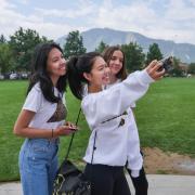 Three students taking a selfie together in front of the flatirons by farrand field.
