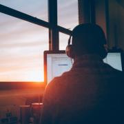 Students sits at his computer with headphones on as the sun sets in the window.