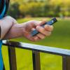 Person holding a vape pen outside in front of a grassy lawn.