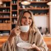 Photo of a young woman holding up a coffee while smiling.