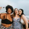 Photo of a group of friends with different body sizes taking a selfie on the beach in their bathing suits.