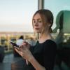 Photo of a student looking at her phone while standing outside on a balcony just before sunset.