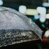 Photo of someone standing in the rain with an umbrella at night.