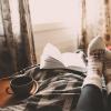 Photo of a person snuggled up with a dog, a book and cozy socks.