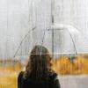 Woman in yellow rain jacket standing with a clear umbrella in the rain.